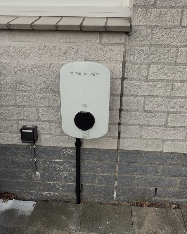 Laadpaal aan de buitenmuur van een woning, met de kabel weggewerkt in een goot.