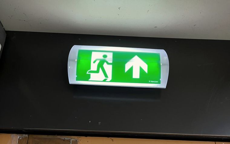 Groen verlicht vluchtwegbordje boven een deur, aangesloten op de noodverlichting.
